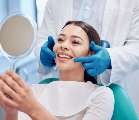 Woman smiling in hand-held mirror in dentist office after procedure